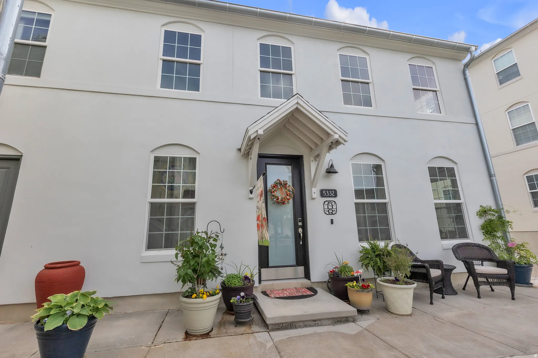 Stucco exterior featuring arched windows, a covered entry with a decorative overhang, a dark-paneled door with a glass insert, and a concrete patio