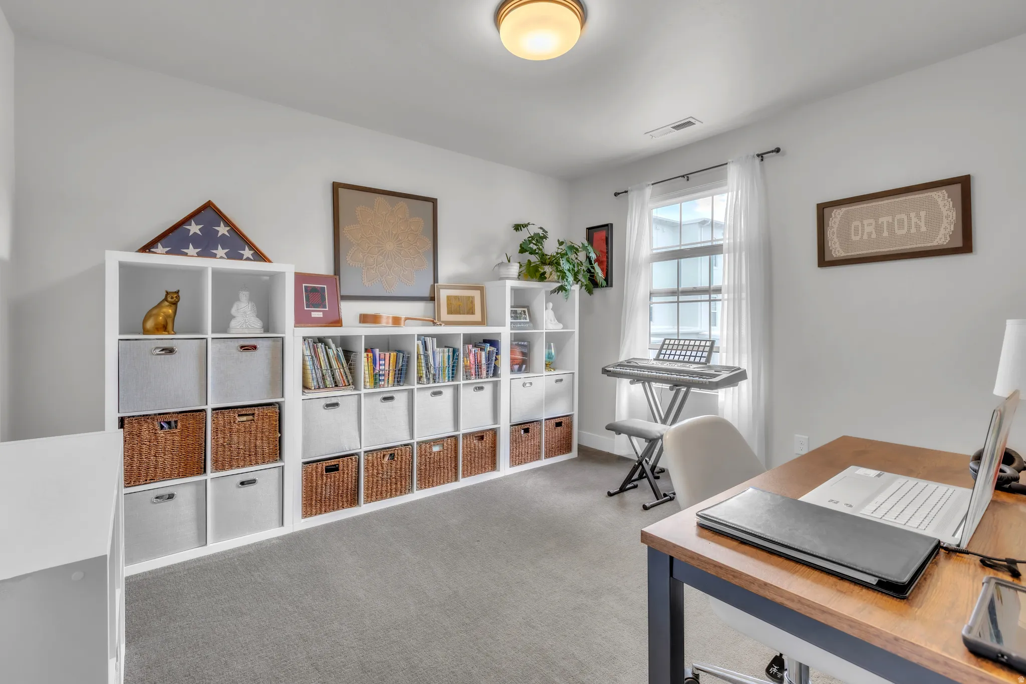 Carpeted room featuring a window with white sheer curtains, a built-in overhead light fixture, and a white wall