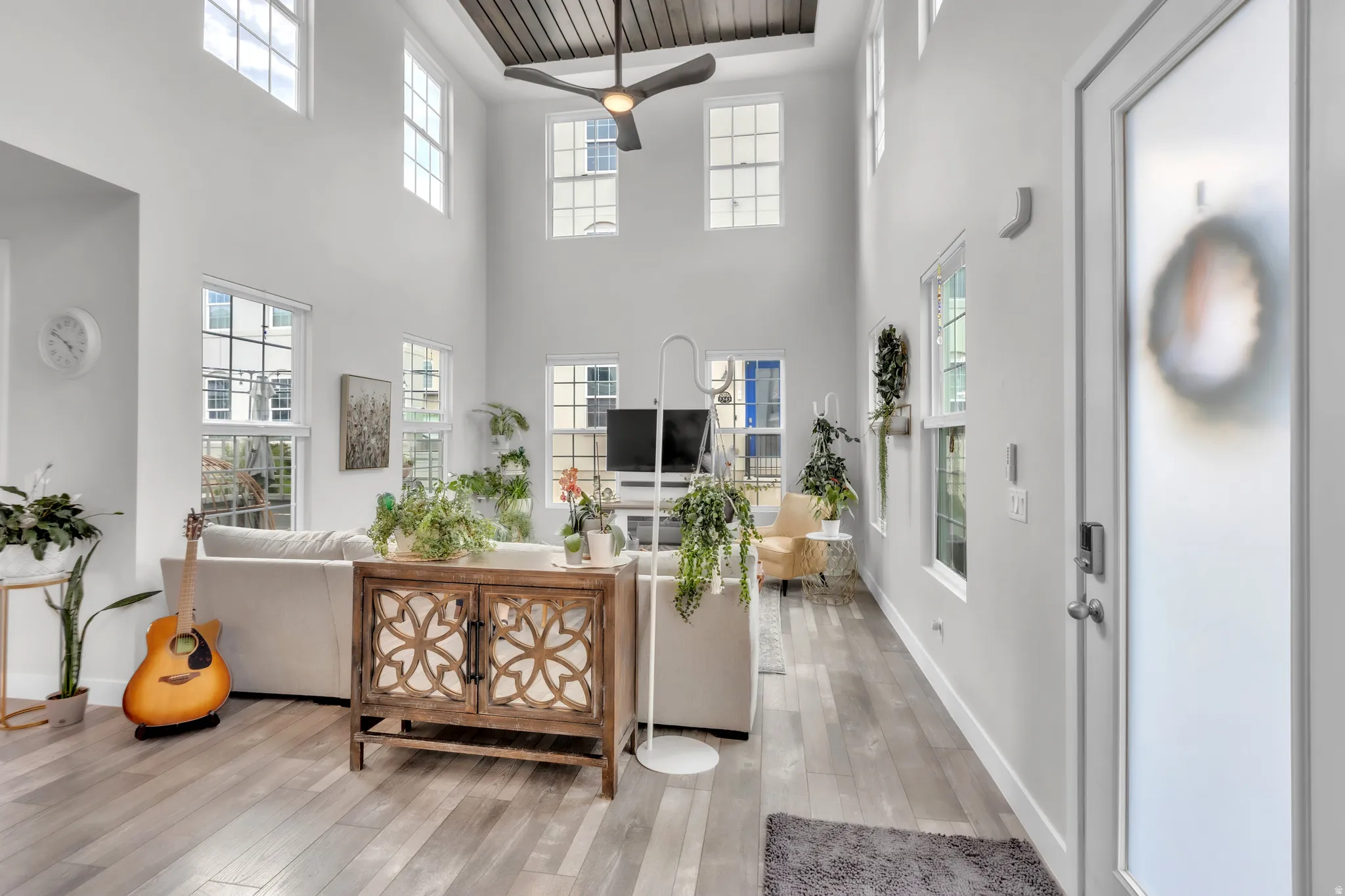Spacious living area featuring high ceilings, numerous windows, wood-finish flooring, and a ceiling fan with integrated lighting