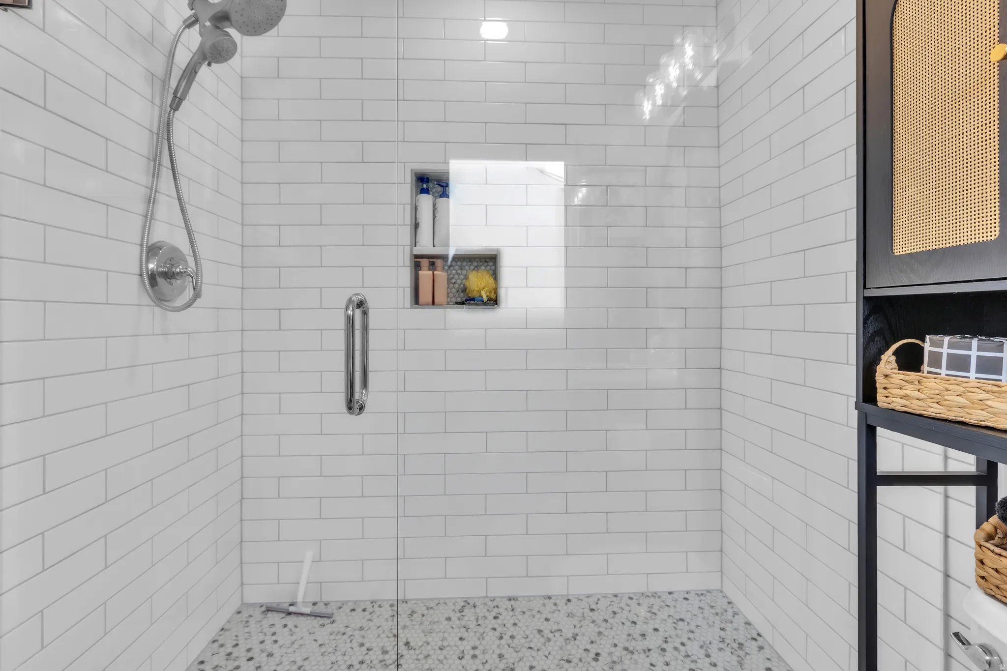 Walk-in shower with white subway tile walls, polished chrome dual shower head, and a built-in shower niche with mosaic tile backing
