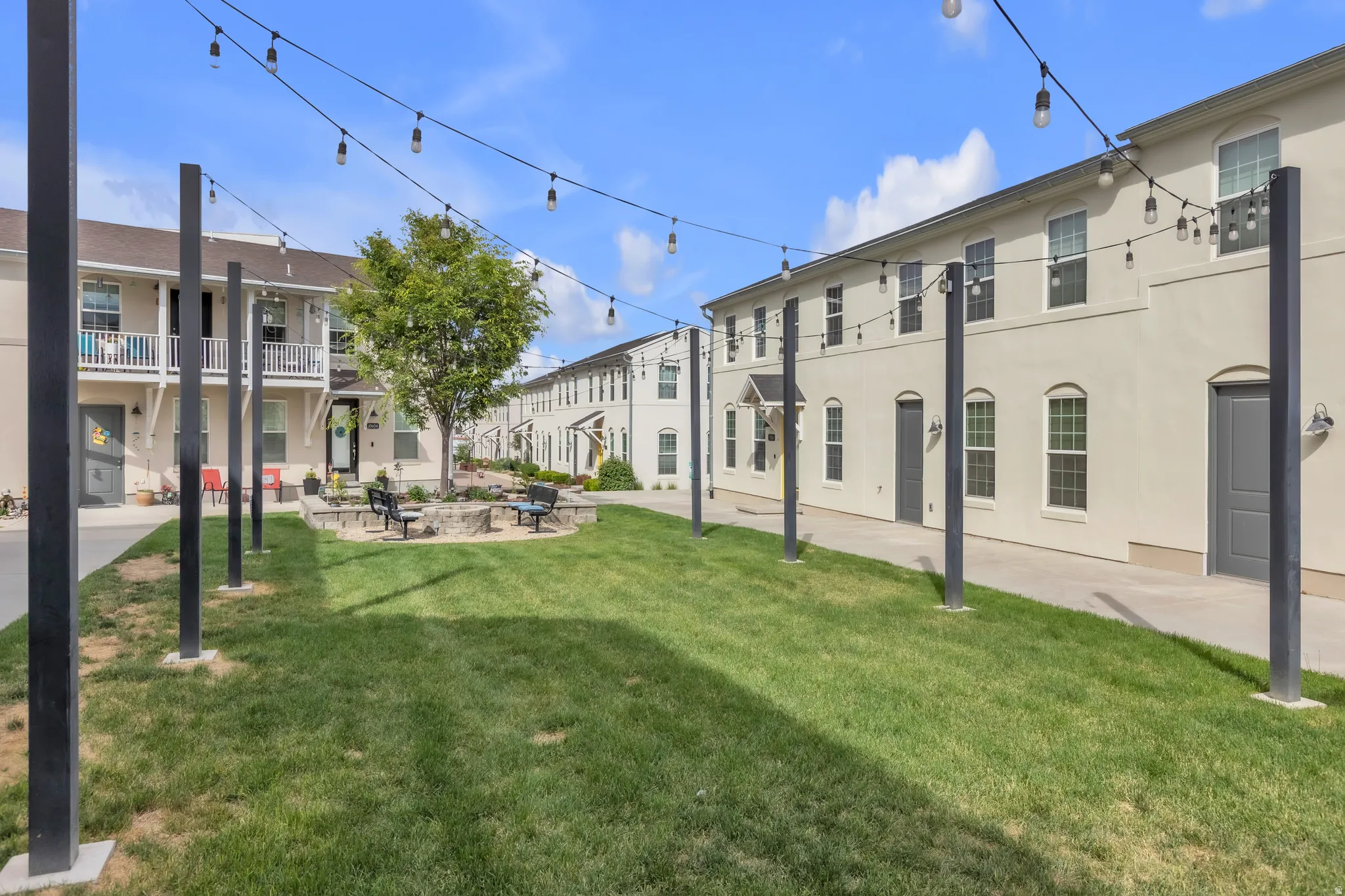 Central green space featuring string lighting, manicured lawn, and a stone-edged planting area with a mature tree