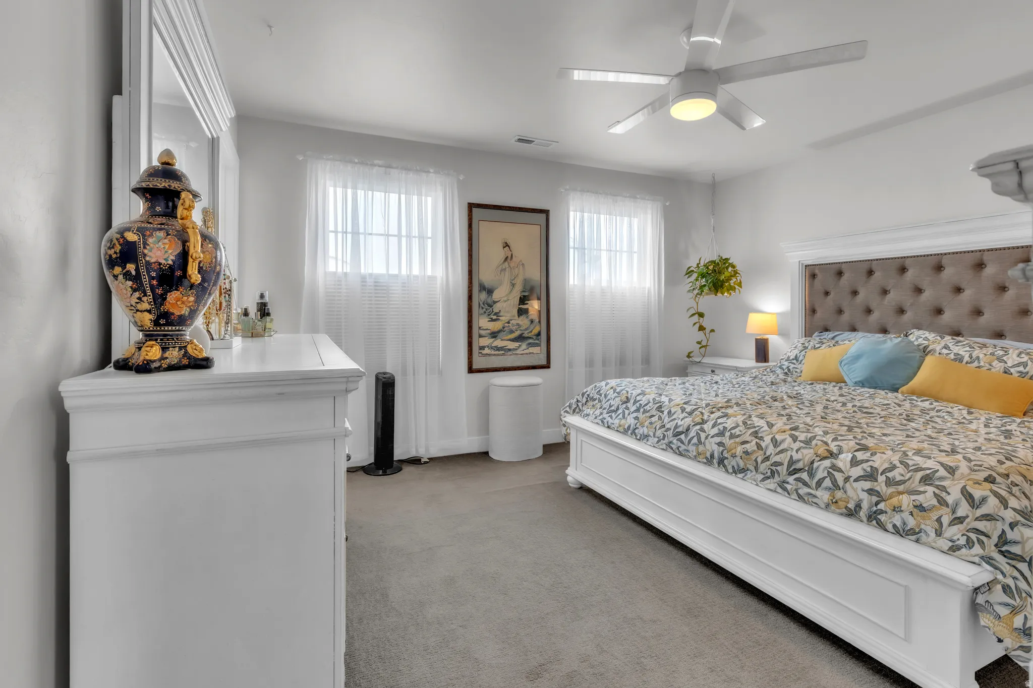 Carpeted room featuring a white paneled bed frame with a tufted headboard, two windows, and an overhead ceiling fan with integrated lighting