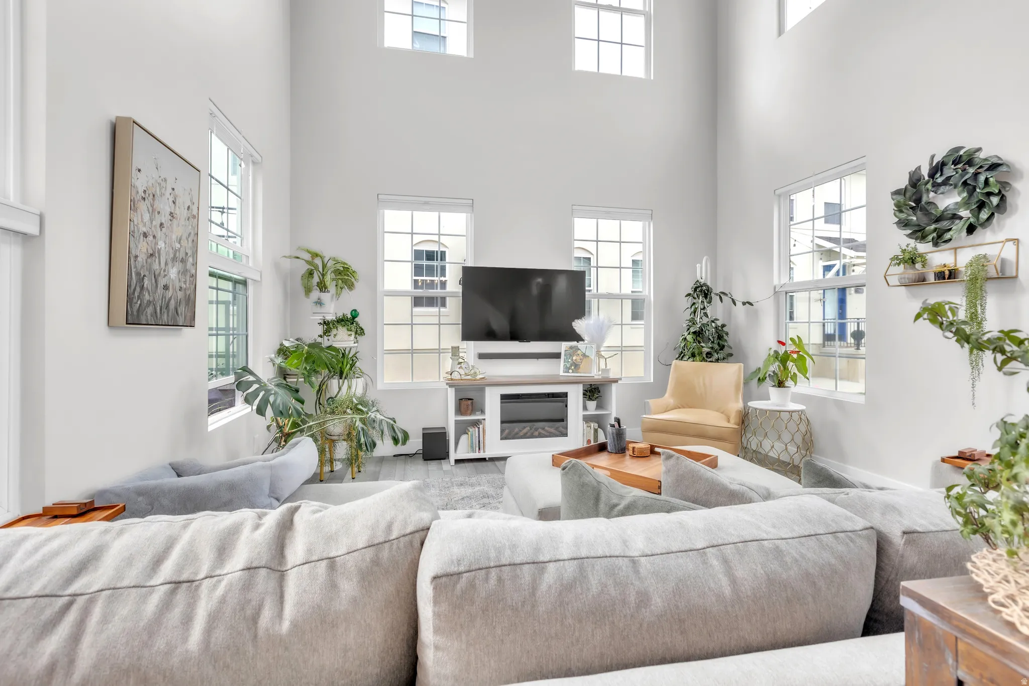 Spacious living area featuring high ceilings, multiple windows with grid patterns, light-toned wall finishes, and dark wood-finish flooring