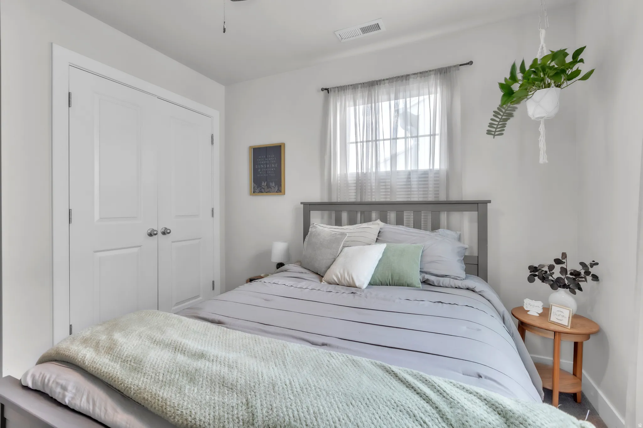 Bedroom featuring a window with sheer curtains, a gray slatted headboard, and a double-door closet with polished chrome hardware