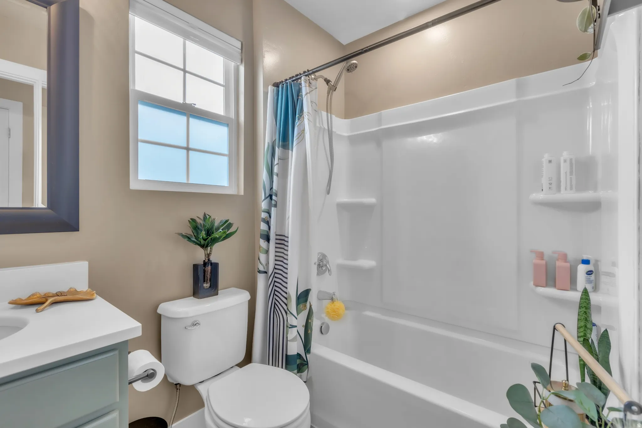 Bathroom featuring a combination bathtub and shower, a single window with blinds, a toilet, and a vanity with a white countertop and basin sink