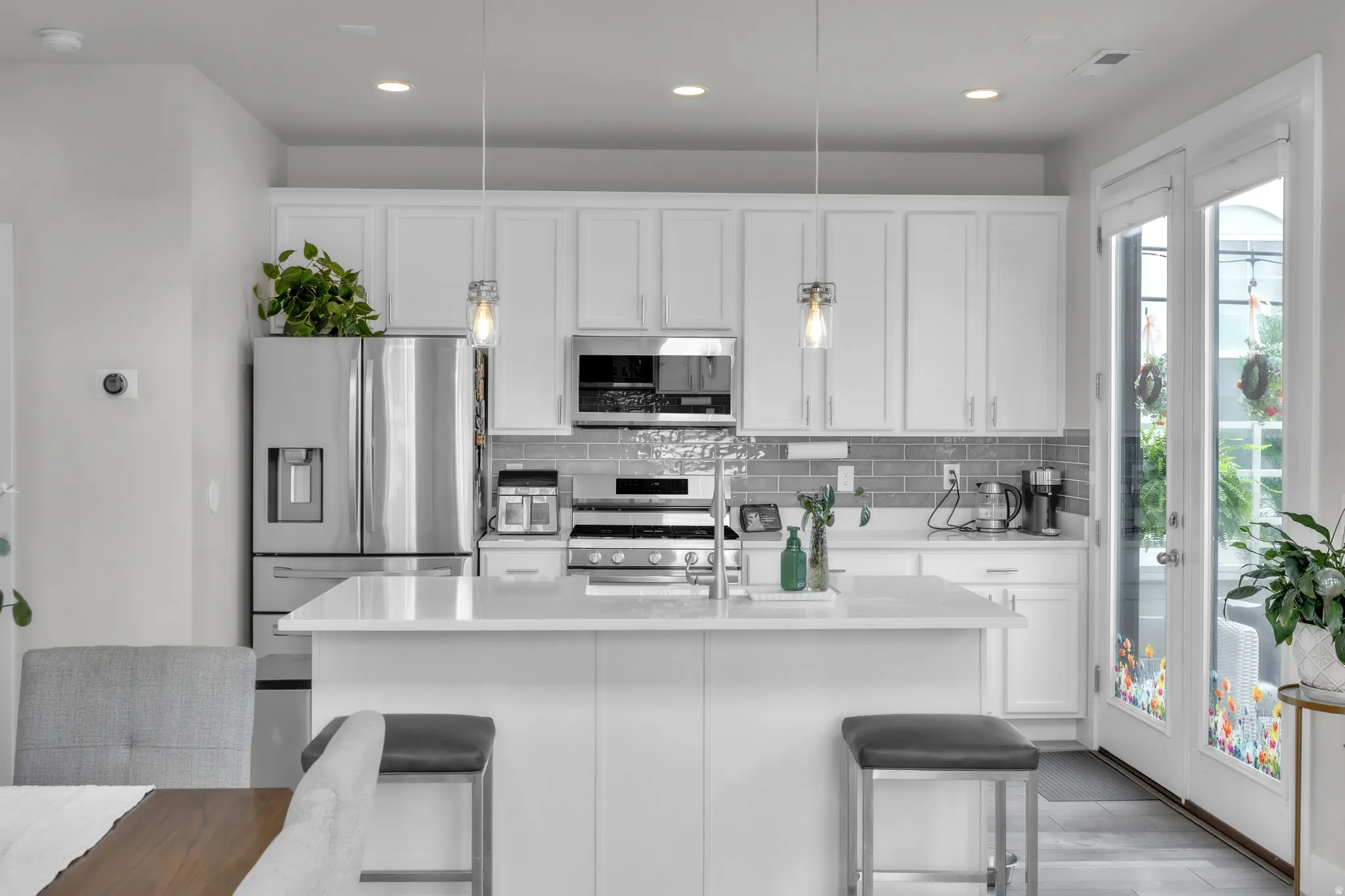 Kitchen featuring white shaker-style cabinetry, stainless steel appliances, a center island with pendant lighting, a tile backsplash, and a glass-paneled door