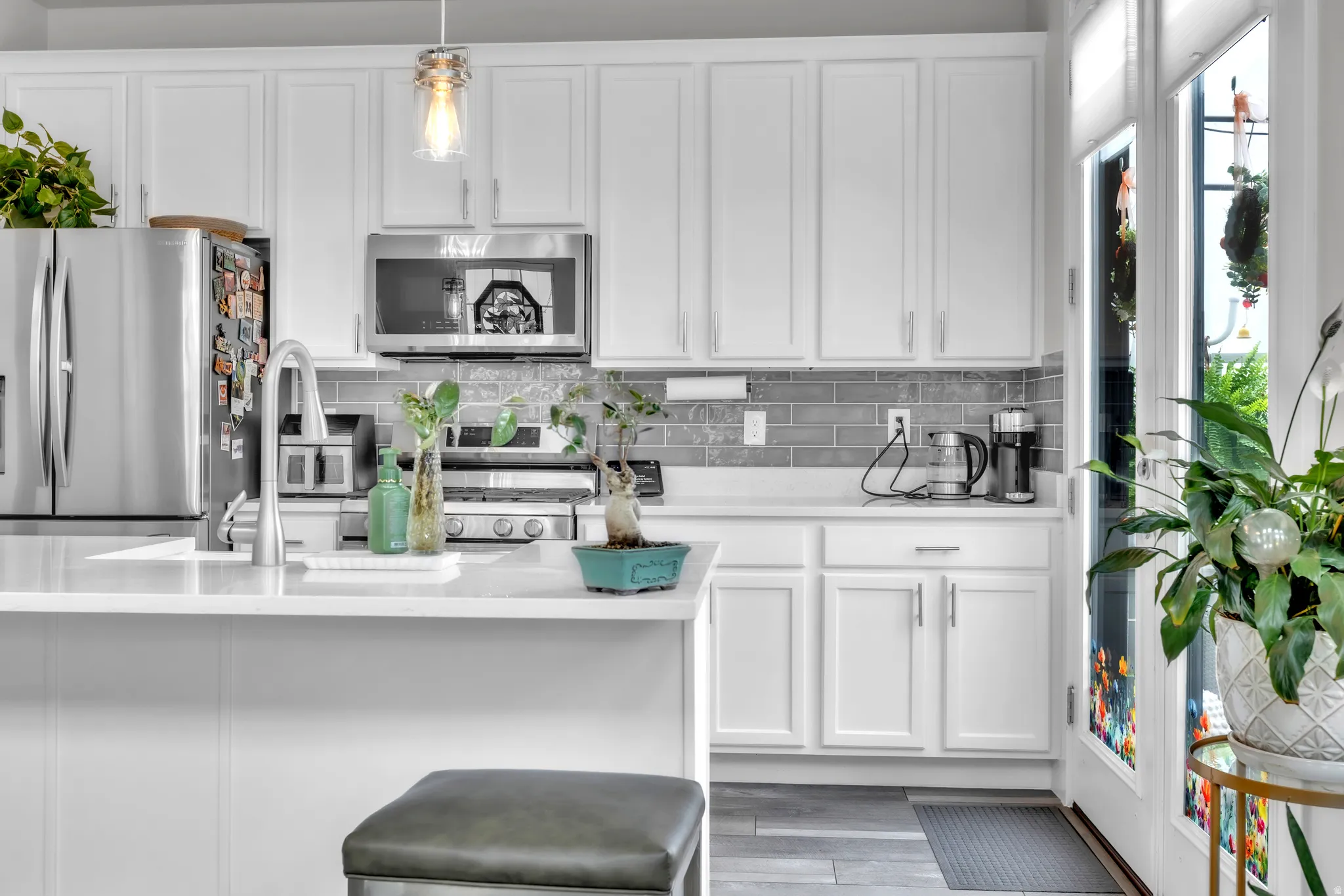 White cabinetry kitchen featuring a large island with an undermount sink, stainless steel appliances, grey subway tile backsplash, and light-colored countertops