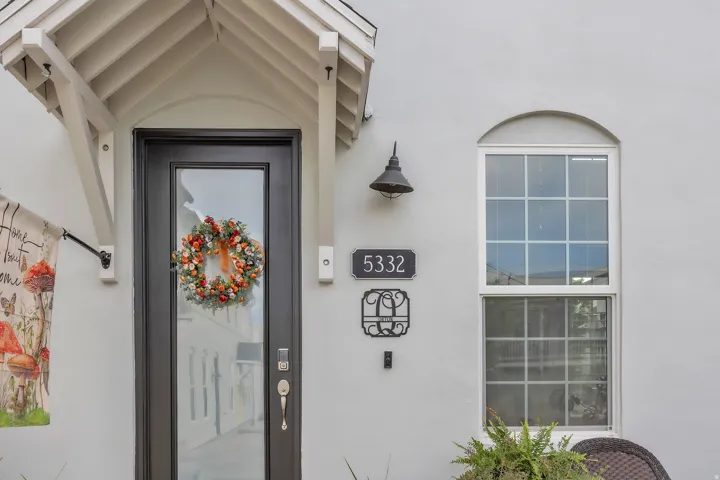 Front entrance featuring a dark-framed glass door, an arched window with grid panes, a protective overhang with exposed rafters, and an exterior wall light fixture