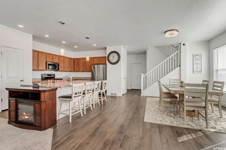 Open concept living space featuring wood-finish flooring, a kitchen island with seating, stainless steel appliances, a staircase with white balusters, and a dining area with a chandelier