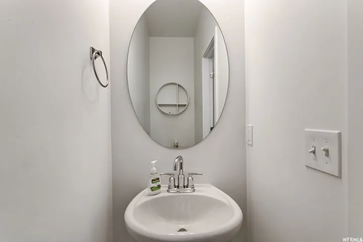 Pedestal sink with chrome faucet, complemented by an oval wall mirror and a wall-mounted towel ring