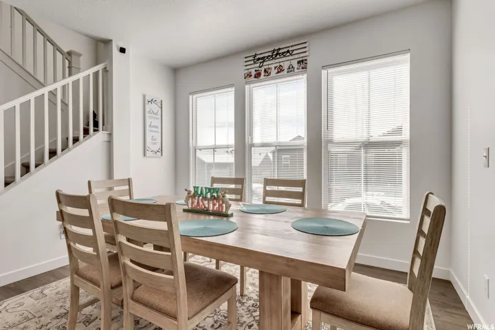 Dining area featuring wood-finish flooring, a white staircase with wood treads, and three large windows fitted with blinds