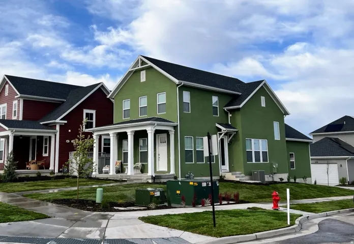 Green stucco exterior with white trim, a covered front porch featuring white columns, and a dark shingle roof