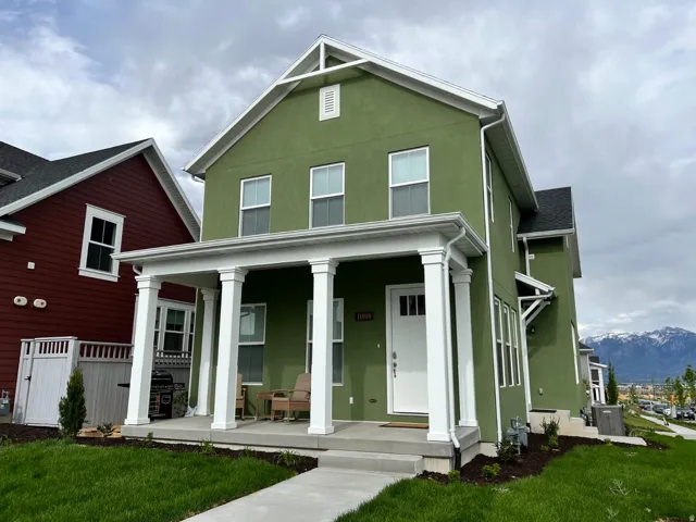 Two-story stucco home featuring a covered front porch with four white columns, white trim throughout, a concrete walkway, and a manicured lawn