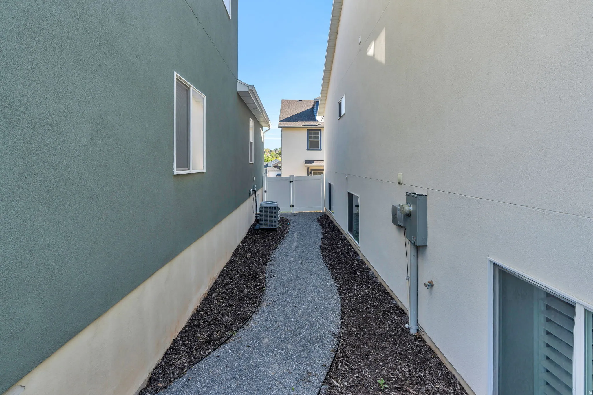 Landscaped side yard featuring a gravel pathway, dark mulch borders, and a white vinyl privacy fence