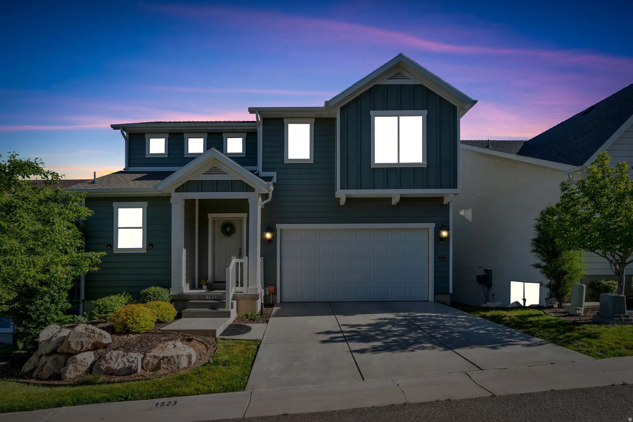 Two-story residence featuring a two-car garage, covered porch entry, board and batten accents, and rock landscaping