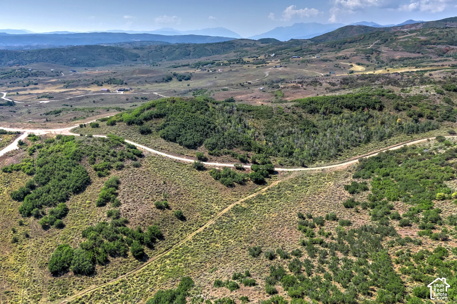 Expansive mountain landscape featuring varied terrain, natural vegetation, and a clear sky backdrop