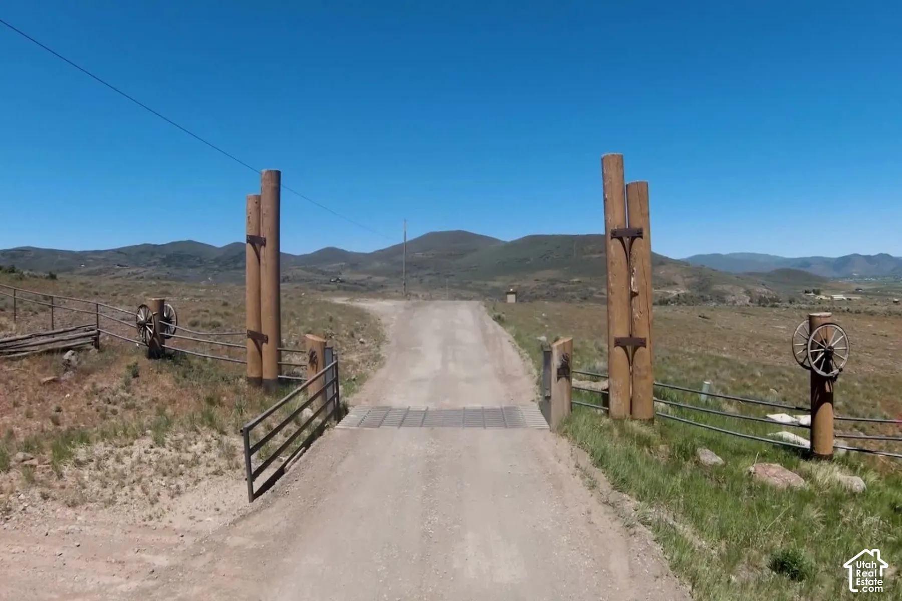 Gated gravel driveway entrance with rustic wood posts, metal fencing, and decorative wagon wheel accents