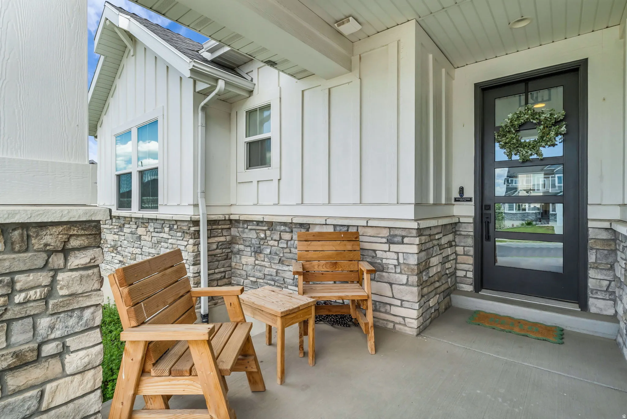 Covered concrete porch featuring a black-framed glass entry door, white board and batten siding, and stacked stone accents