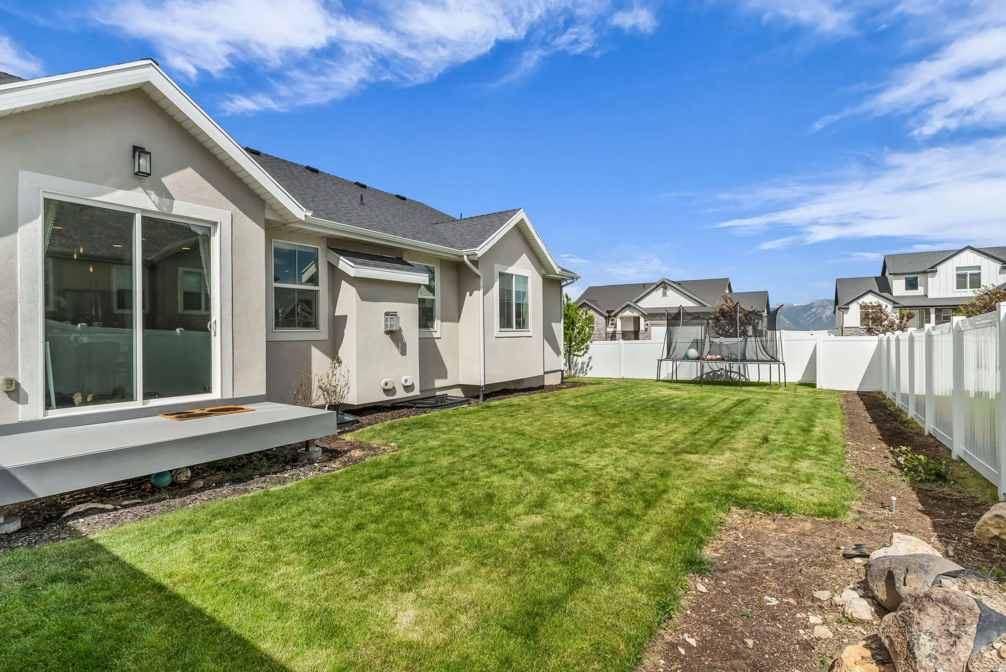 Spacious backyard featuring a manicured lawn, white privacy fencing, and a concrete patio with sliding glass door access