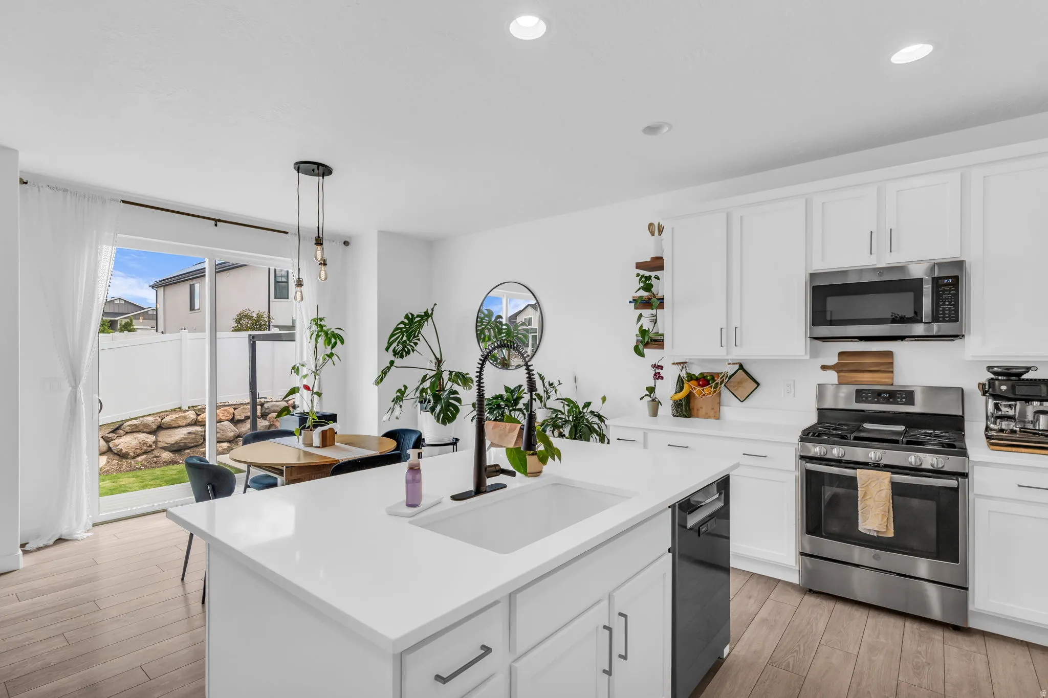Kitchen featuring white cabinetry, stainless steel appliances, a large island with an undermount sink, recessed lighting, and wood-finish flooring