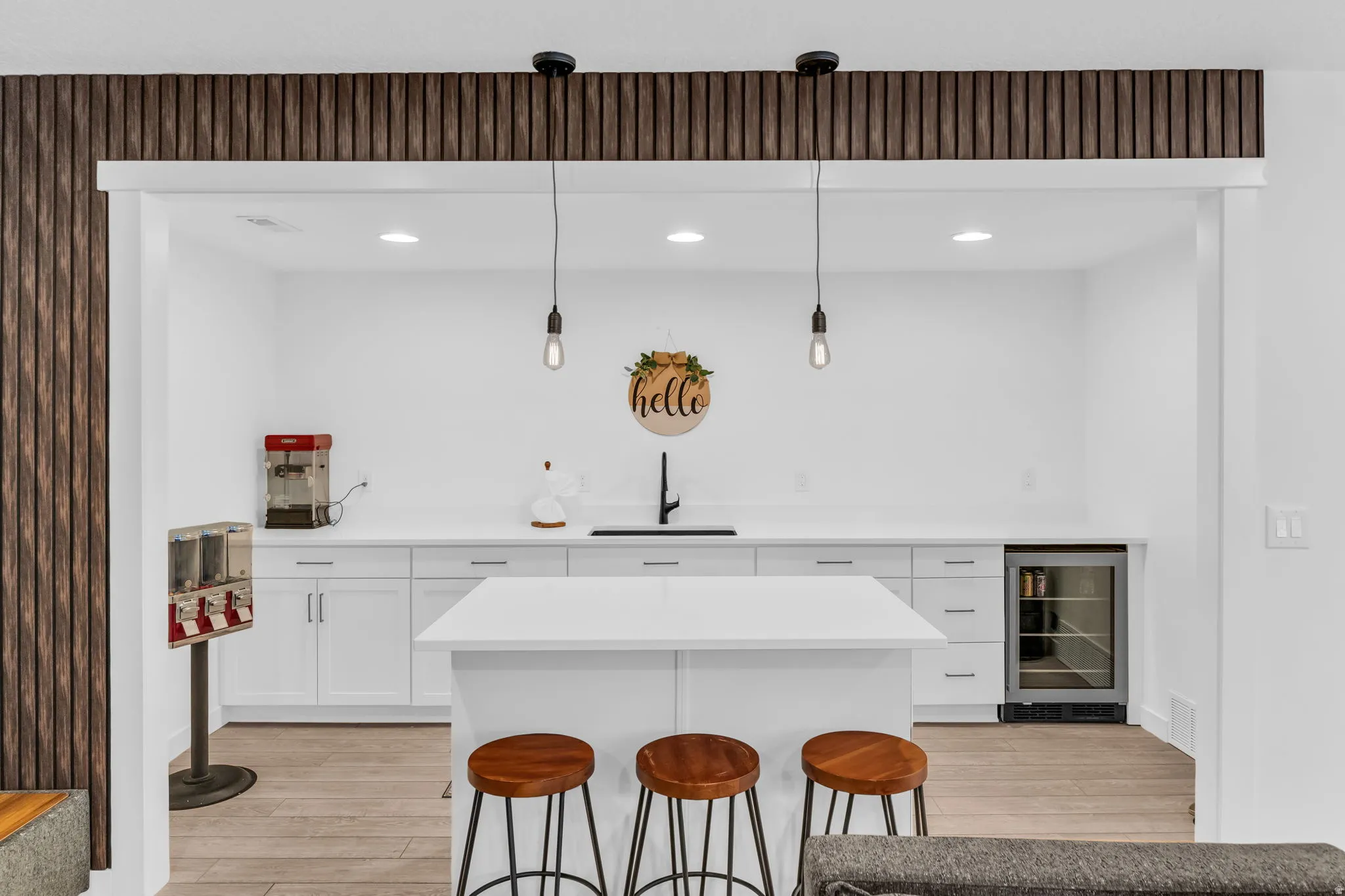 Contemporary wet bar featuring a central island with countertop seating, white shaker-style cabinetry, a built-in beverage refrigerator, and a sleek black faucet