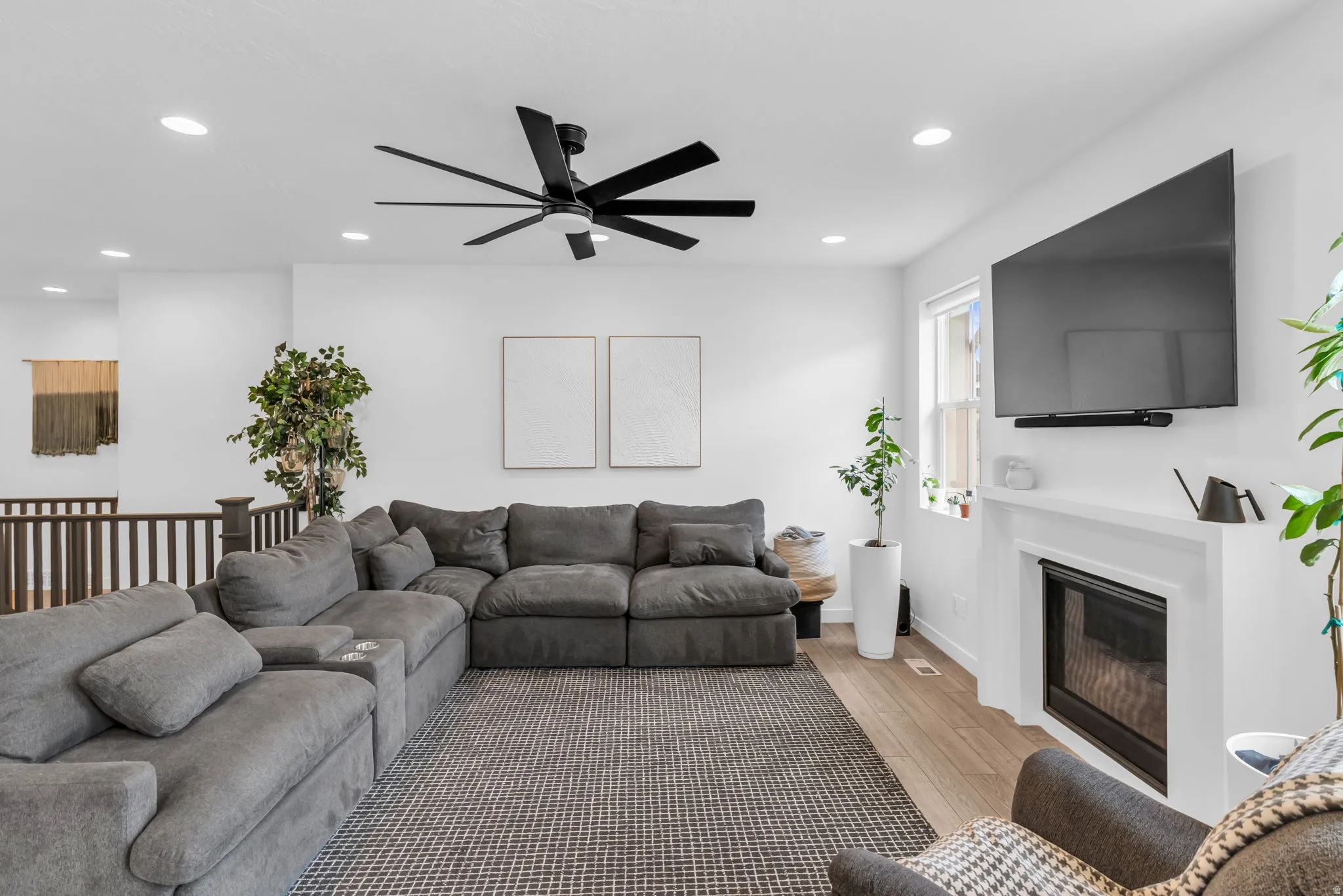 Bright living area featuring recessed lighting, a modern ceiling fan, wood-finish flooring, a white-framed fireplace, and a window providing natural light