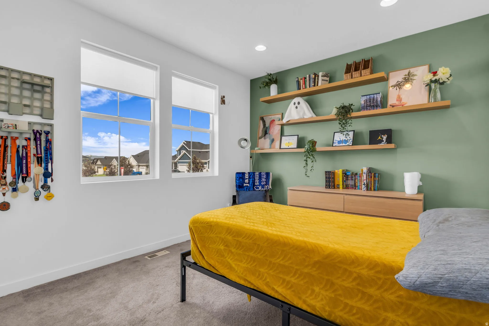 Twin windows with roller shades, recessed lighting, and a green accent wall with multiple wood-finish floating shelves