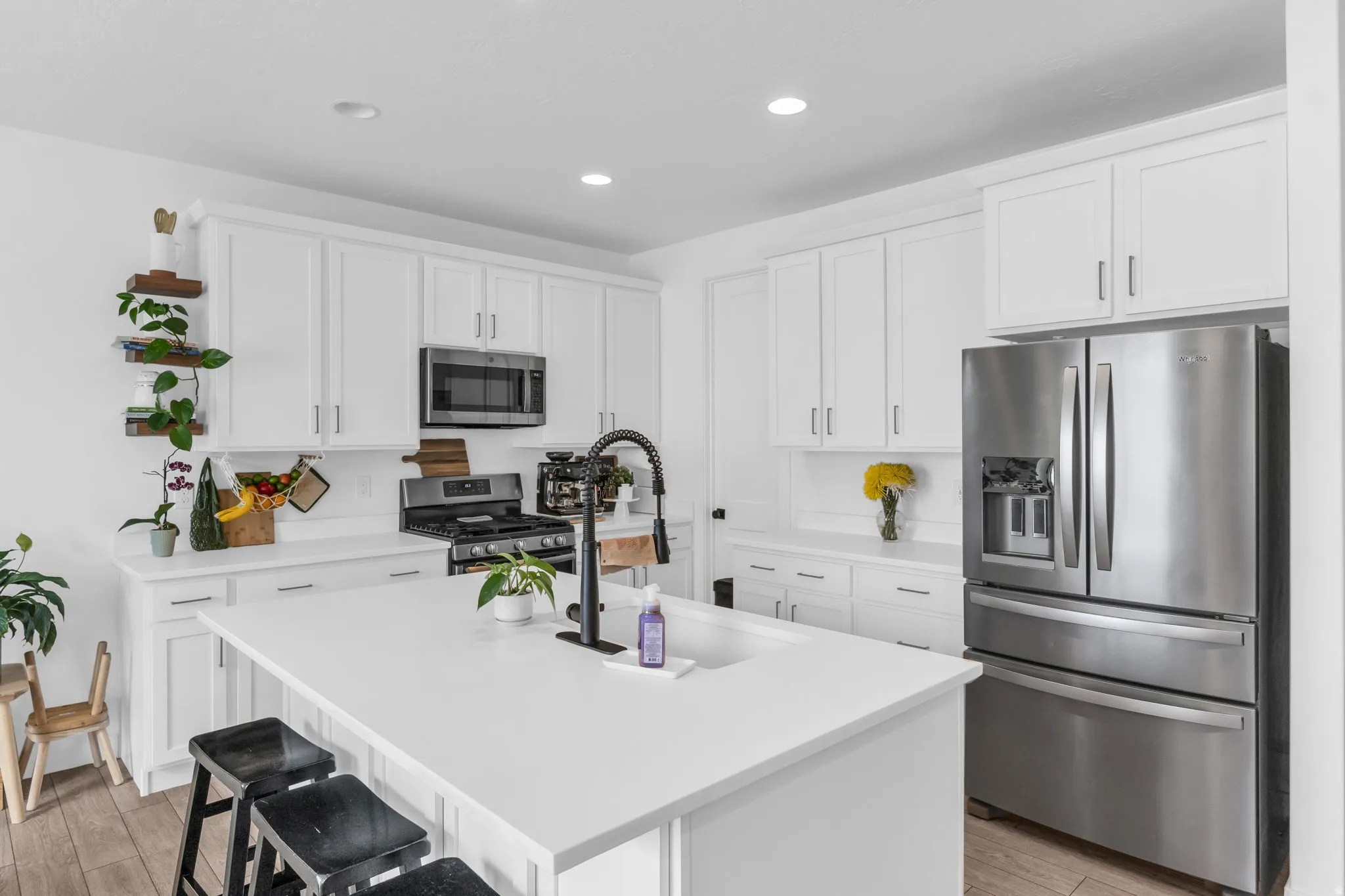 Contemporary kitchen featuring white shaker cabinetry, stainless steel appliances, a center island with sink and seating, and light wood-finish flooring