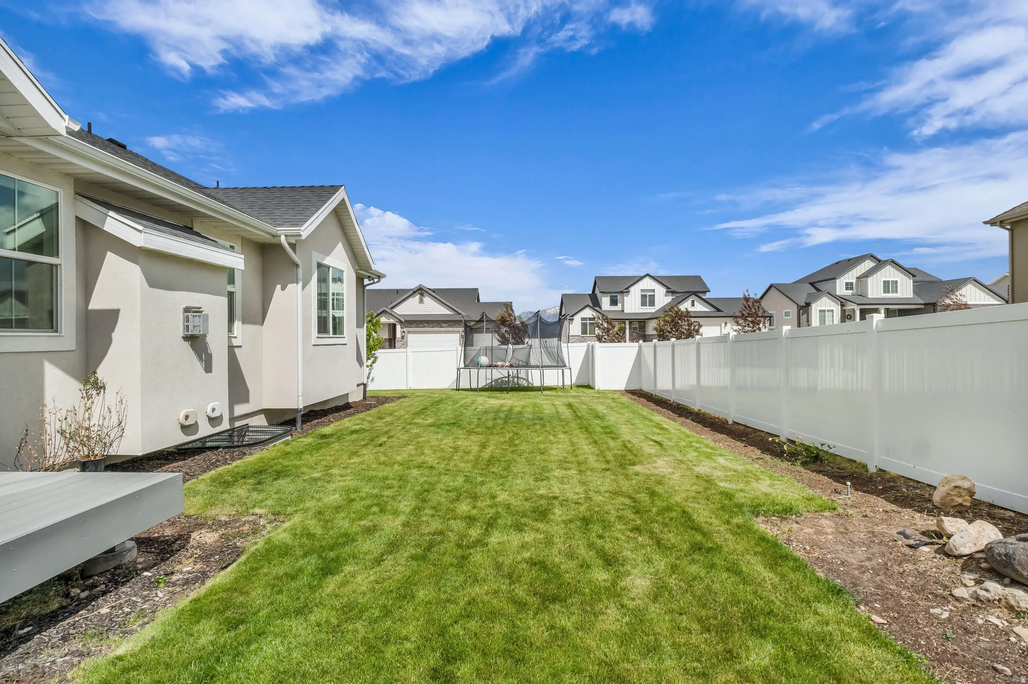 Expansive backyard featuring a manicured lawn, a full white vinyl privacy fence, and a gray composite deck