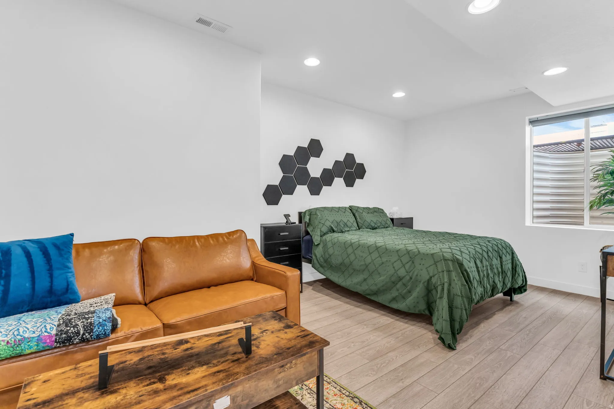 Open-concept living area featuring light wood-finish flooring, recessed lighting, a large window, and crisp white walls