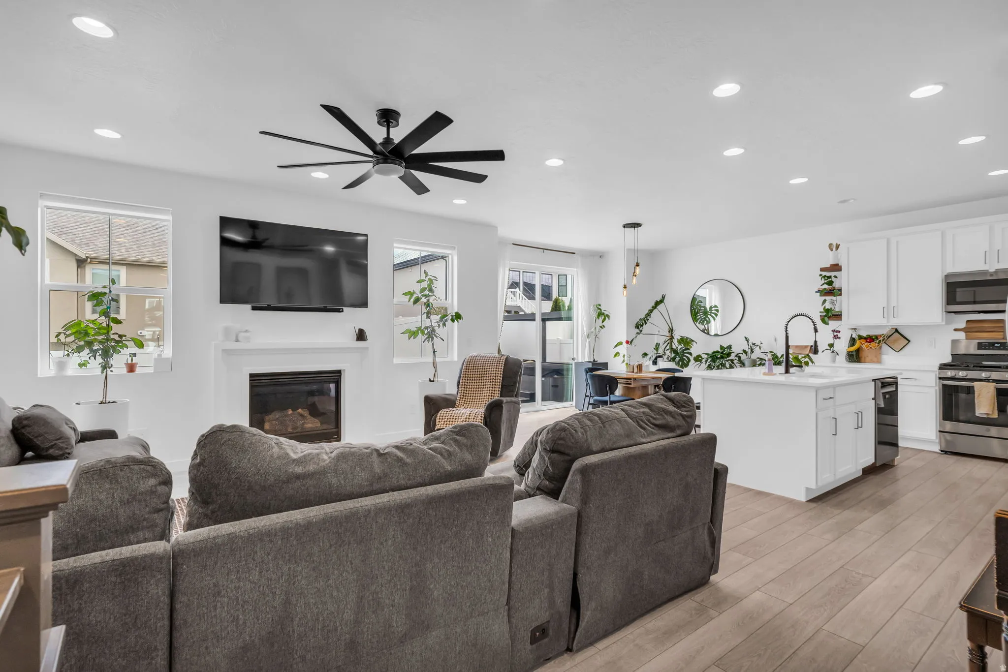 Open-concept living space featuring wood-finish flooring, a contemporary fireplace with a mantel, recessed lighting, and a modern ceiling fan