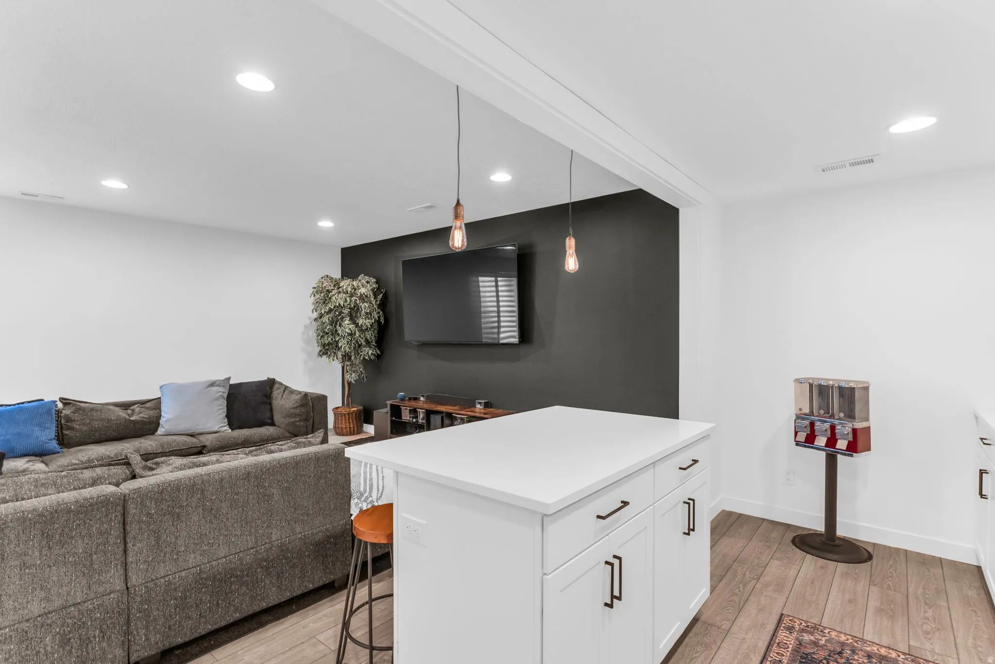 Open-concept entertainment space featuring a white kitchen island with a quartz countertop, recessed lighting, and wood-finish flooring