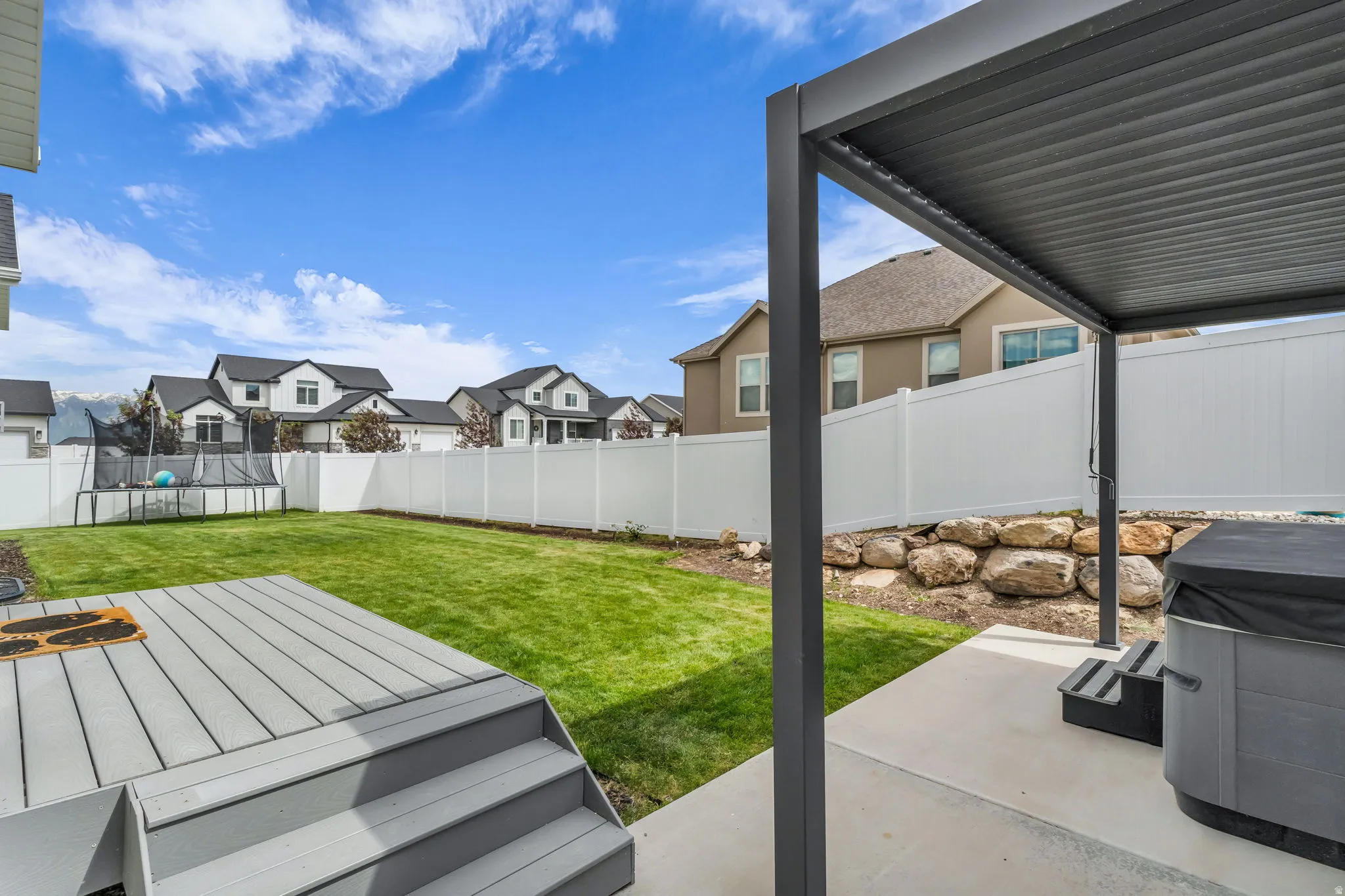 Expansive backyard featuring a large green lawn, a multi-tiered composite deck, and a concrete patio with a modern pergola