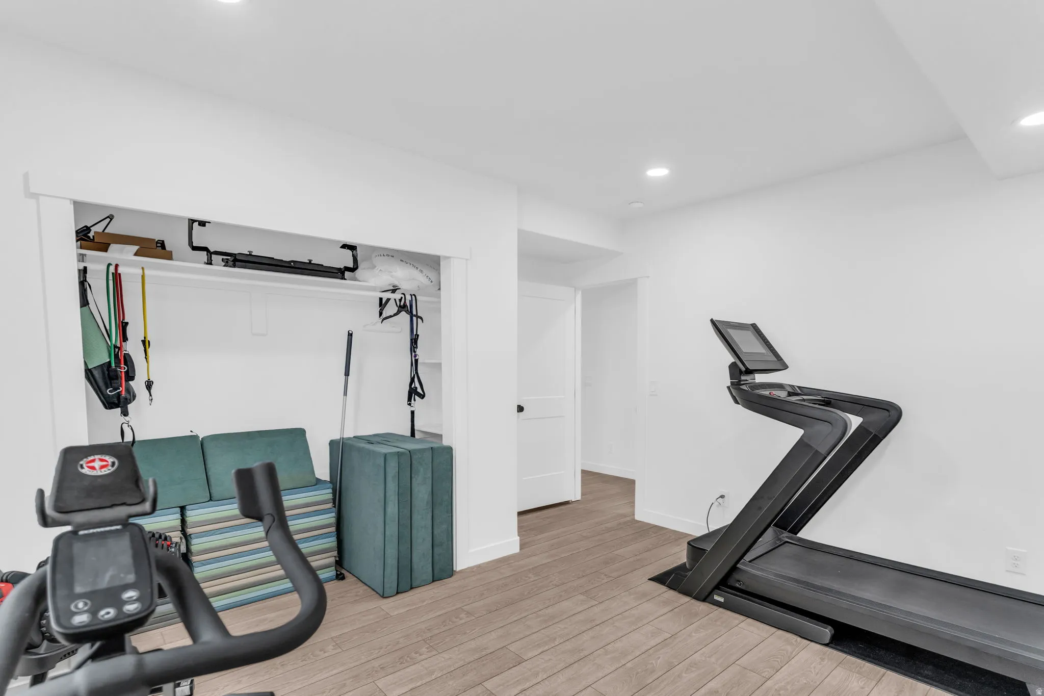 Recessed lighting illuminates a versatile space featuring wood-finish flooring and crisp white walls
