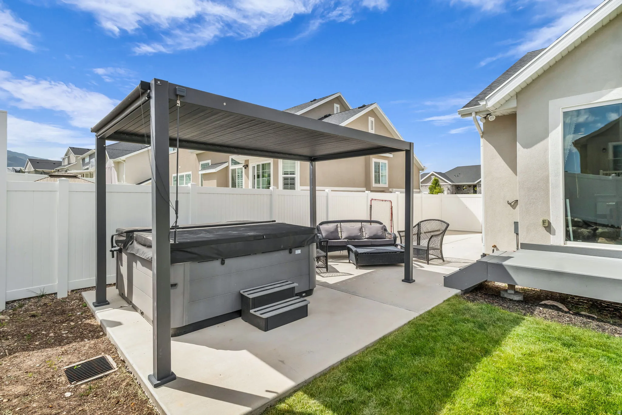 Rear patio featuring a covered hot tub, concrete paving, a privacy fence, and a grass lawn