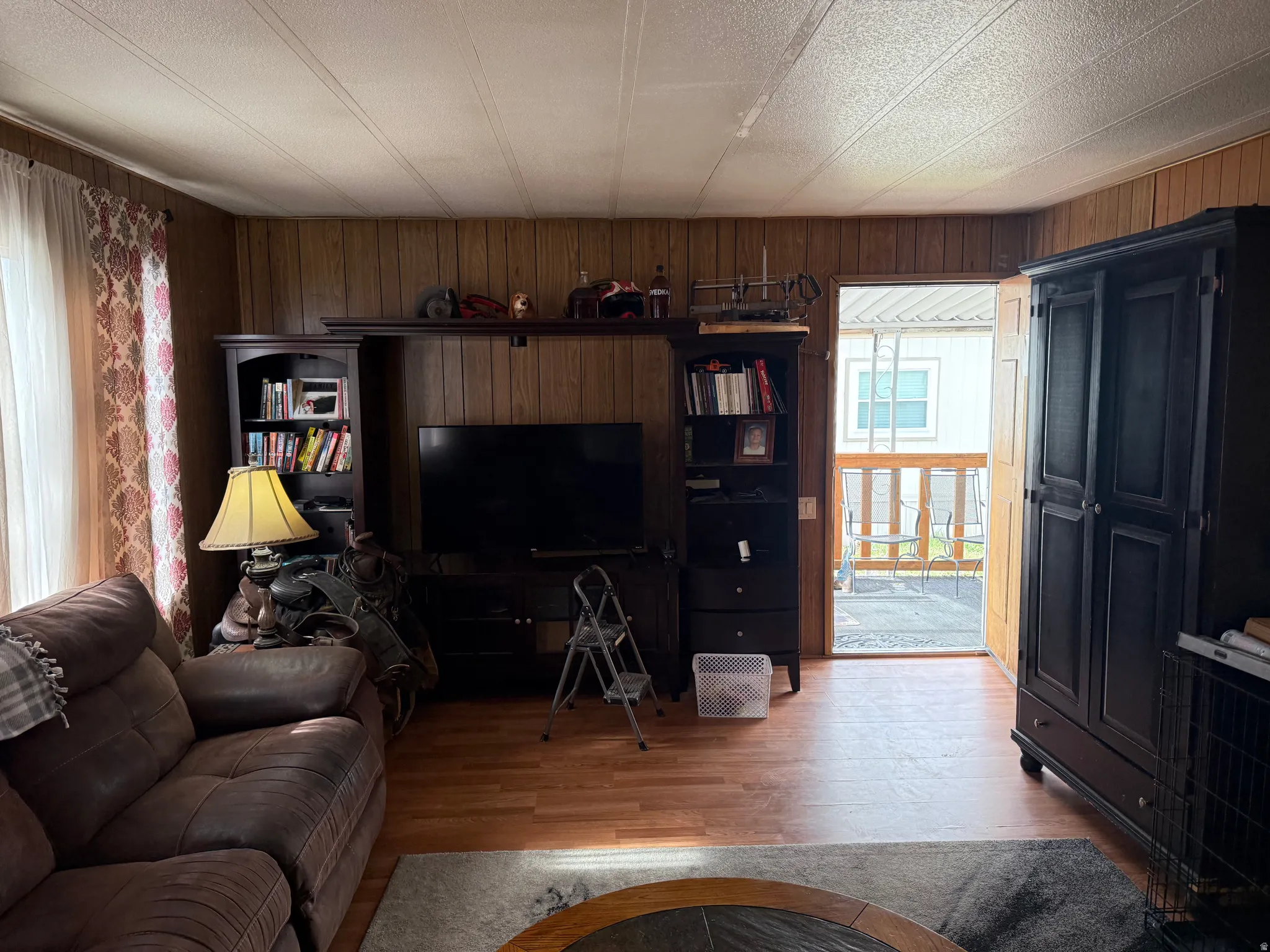 Living area featuring wood-finish flooring, wood panel wall accents, and an exterior door leading to an outdoor deck