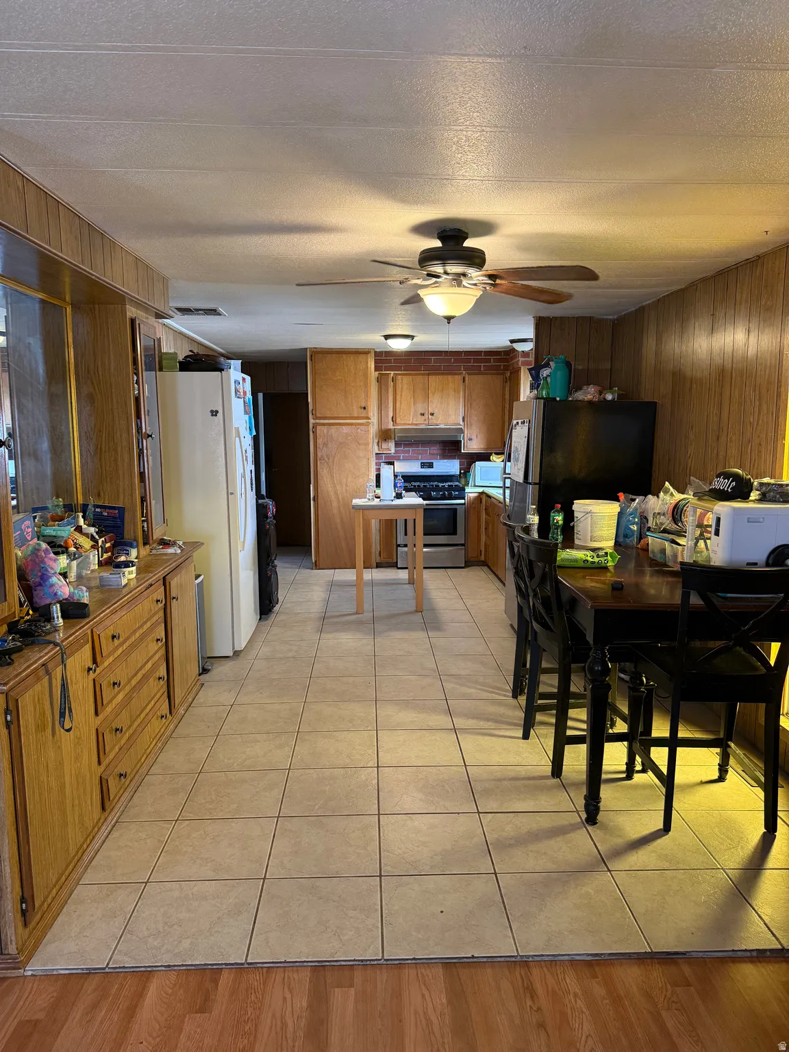 Open-concept living space featuring wood paneling, square tile flooring, a built-in wood-finish credenza, and a ceiling fan with integrated lighting
