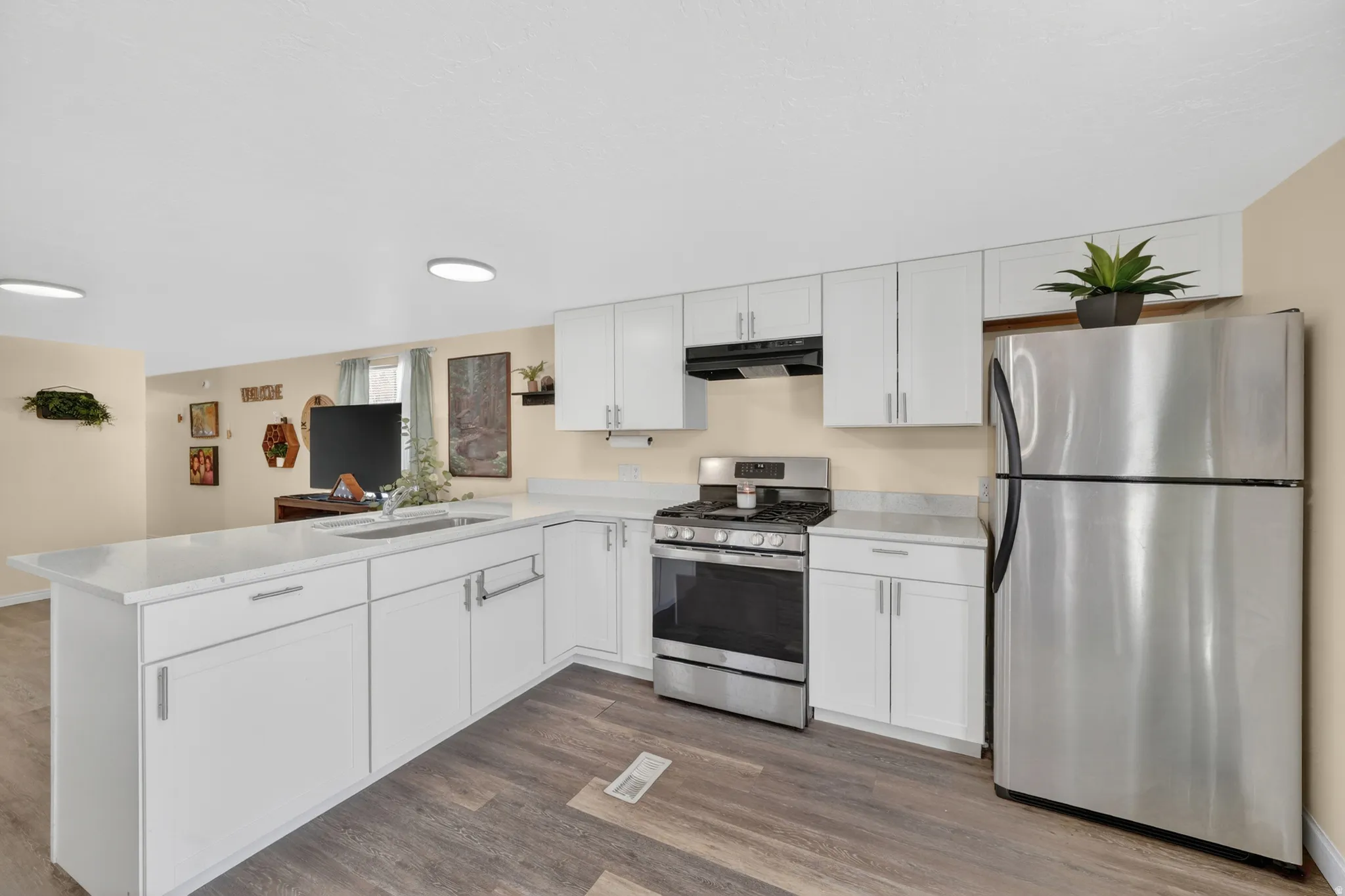 Modern kitchen featuring white cabinetry, light countertops, stainless steel appliances, and wood-finish flooring