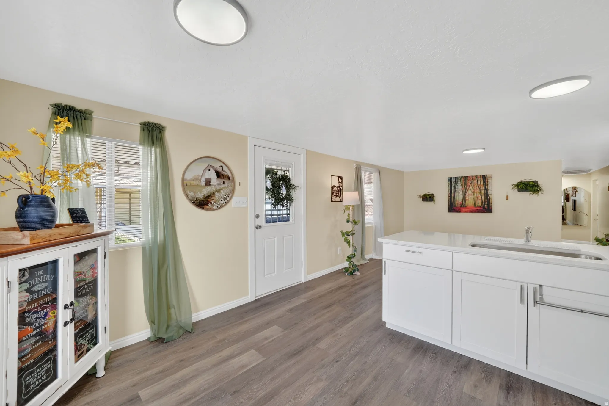 Kitchen area featuring an island with a stainless steel sink, white cabinetry, and a light-toned countertop