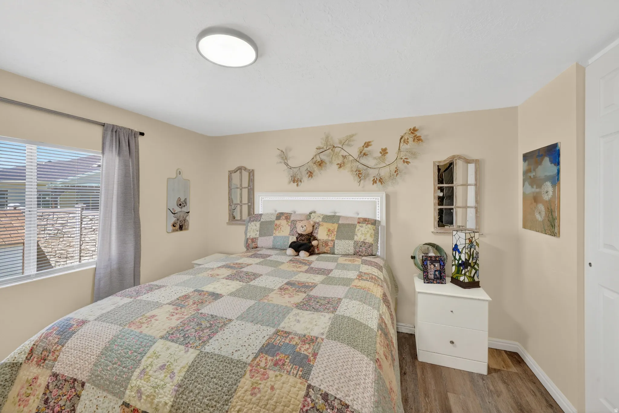 Bedroom with a large window and blinds, featuring wood-finish flooring and light-toned walls