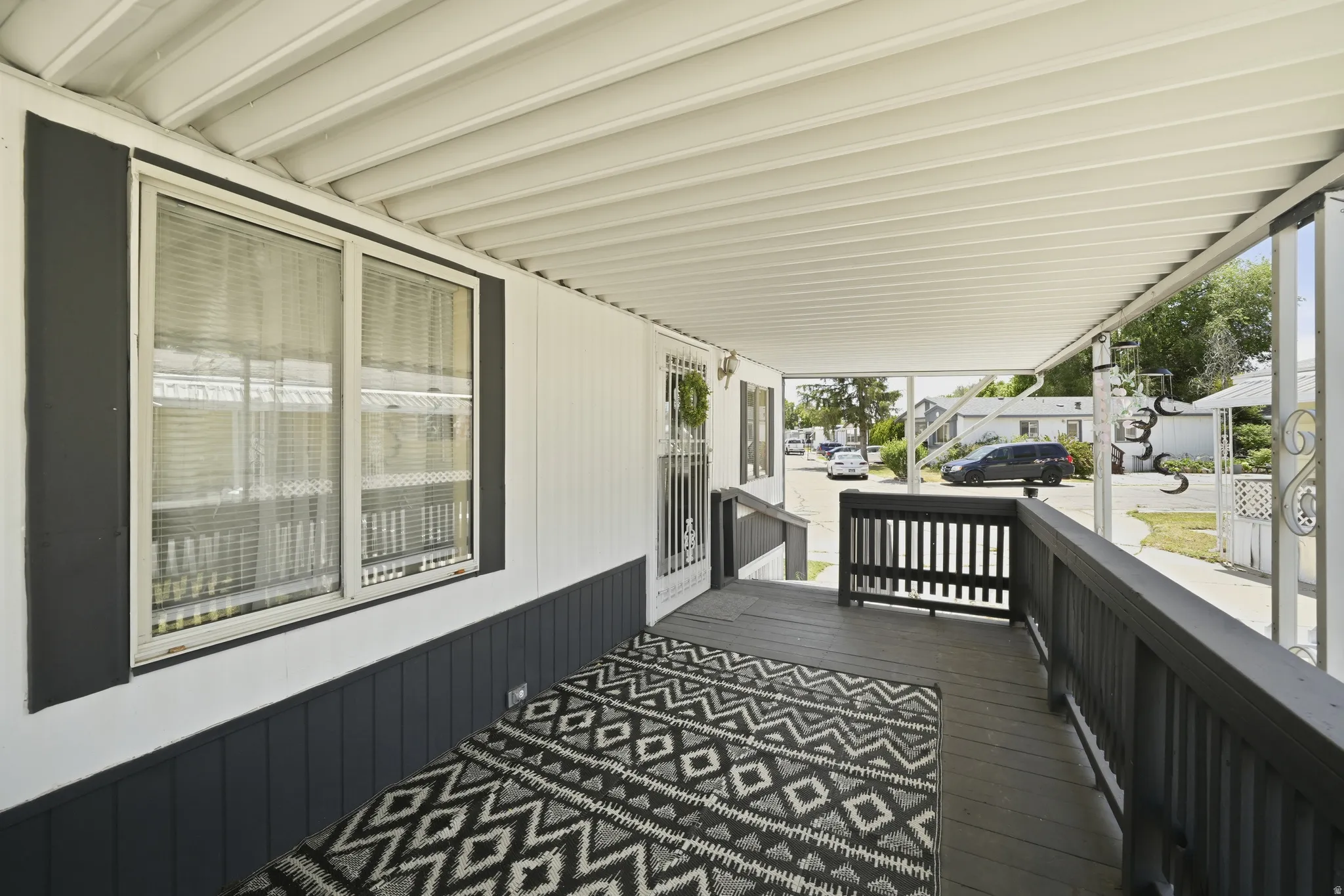 Covered front porch featuring a dark wood-finish deck, white siding, and dark accent trim