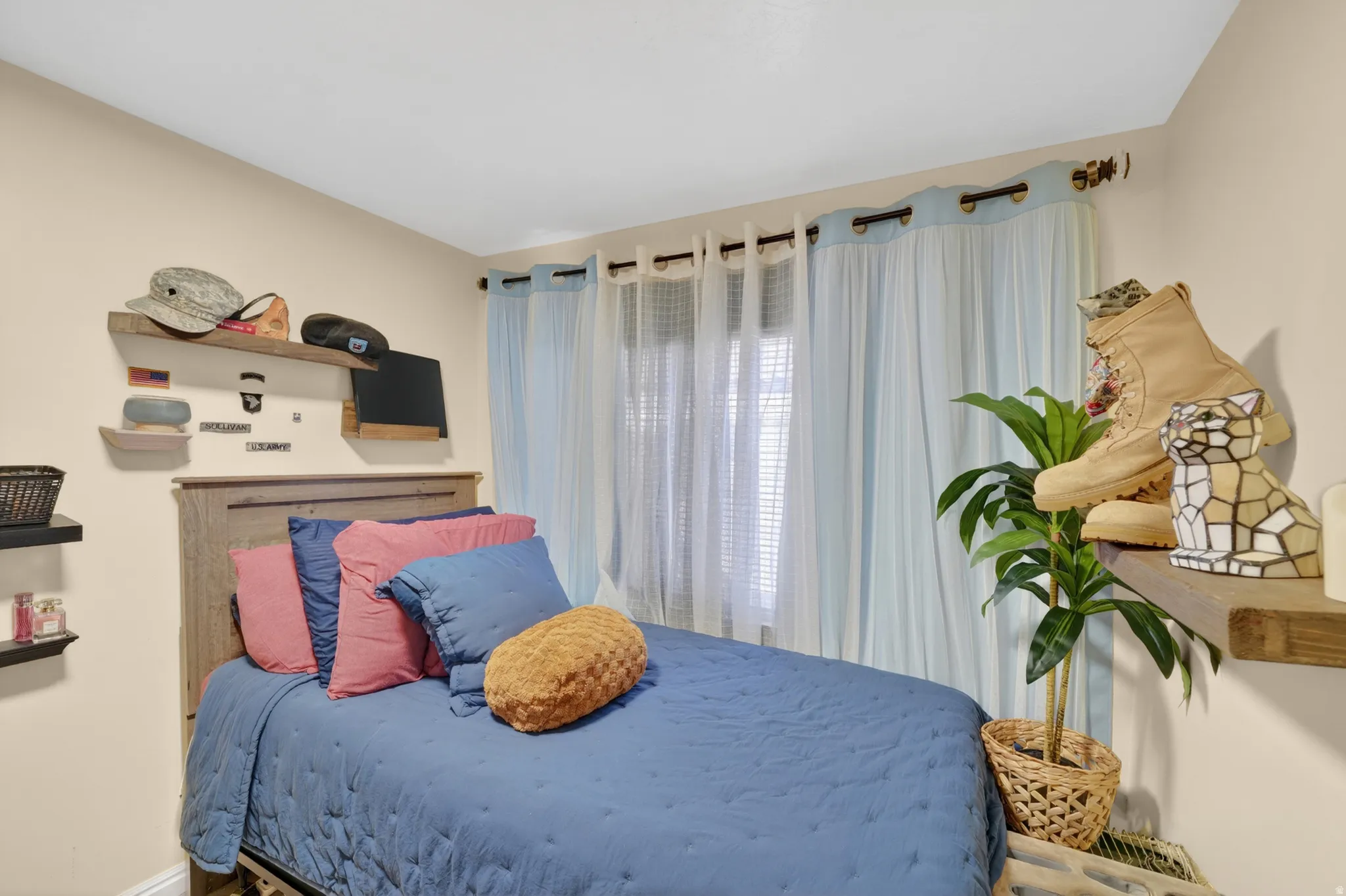 Bedroom with neutral-toned walls, a window featuring light blue and sheer curtains, and a wood-finish headboard