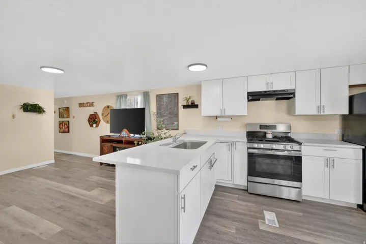 Open-concept kitchen featuring white cabinetry, light countertops, stainless steel appliances, and wood-finish flooring