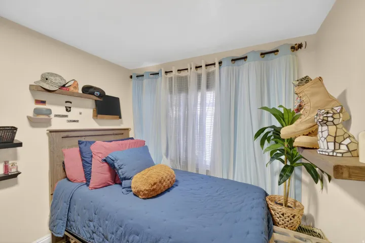 Bedroom with neutral-toned walls, a window featuring light blue and sheer curtains, and a wood-finish headboard