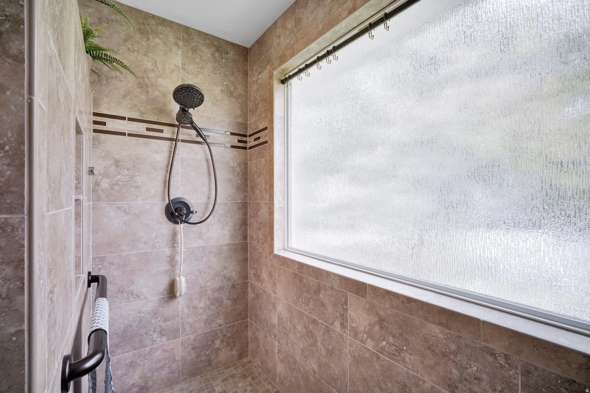 Primary bath shower with floor-to-ceiling textured tile, decorative tile band, built-in recessed shelving, a wide privacy window, and a matte black shower fixture