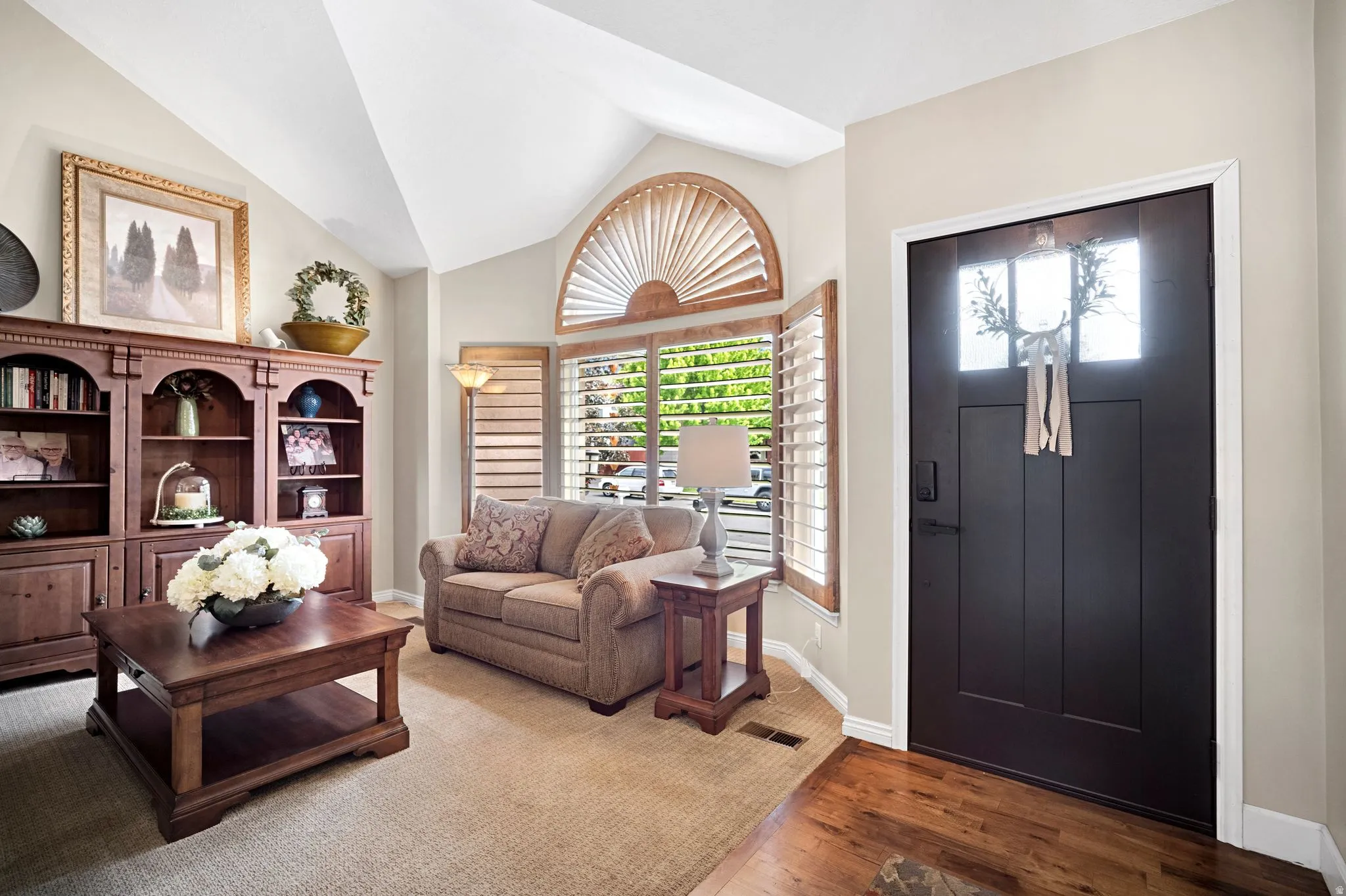 Vaulted ceiling living area featuring neutral carpet with walnut wood entry way.