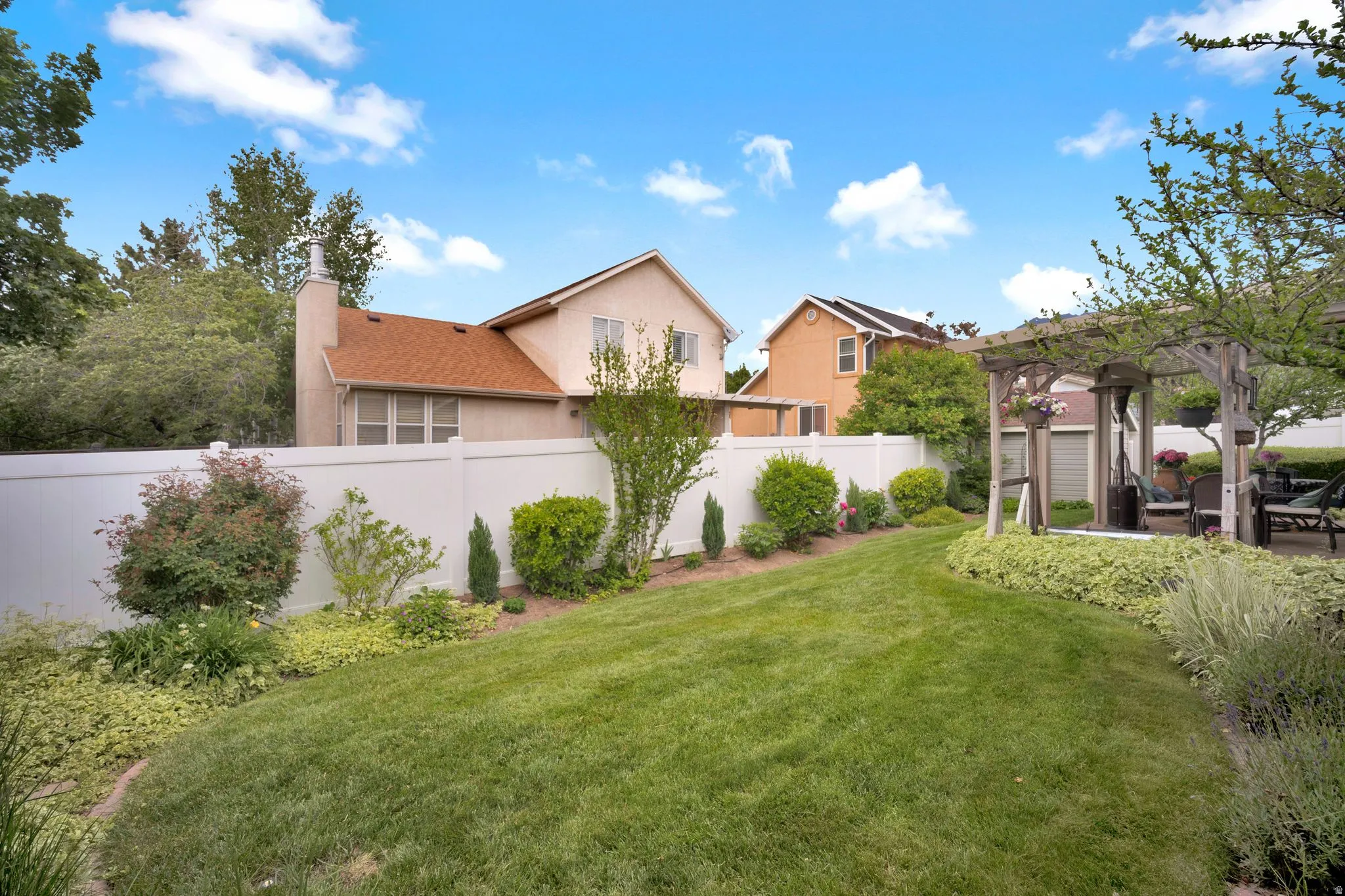 Backyard featuring well maintained bedding areas, vinyl fencing and covered patio.