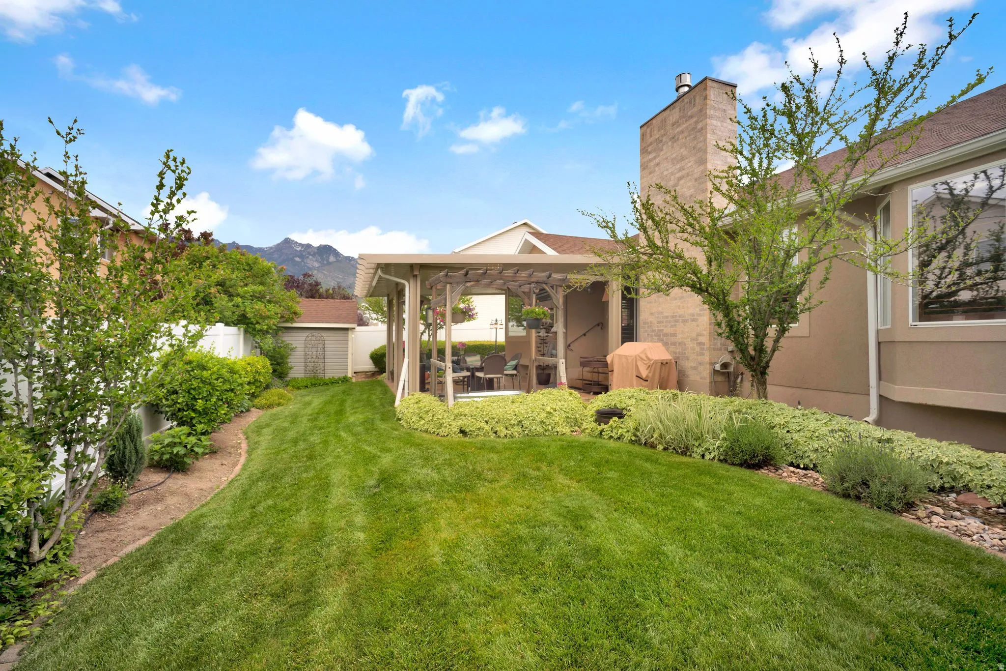 Private backyard featuring a lush lawn, mature landscaping, a covered patio structure, and water feature.
