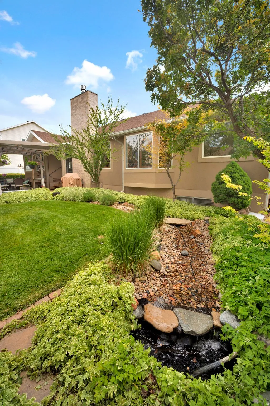 Lush backyard featuring a tranquil rock waterfall, a manicured lawn, and mature trees.