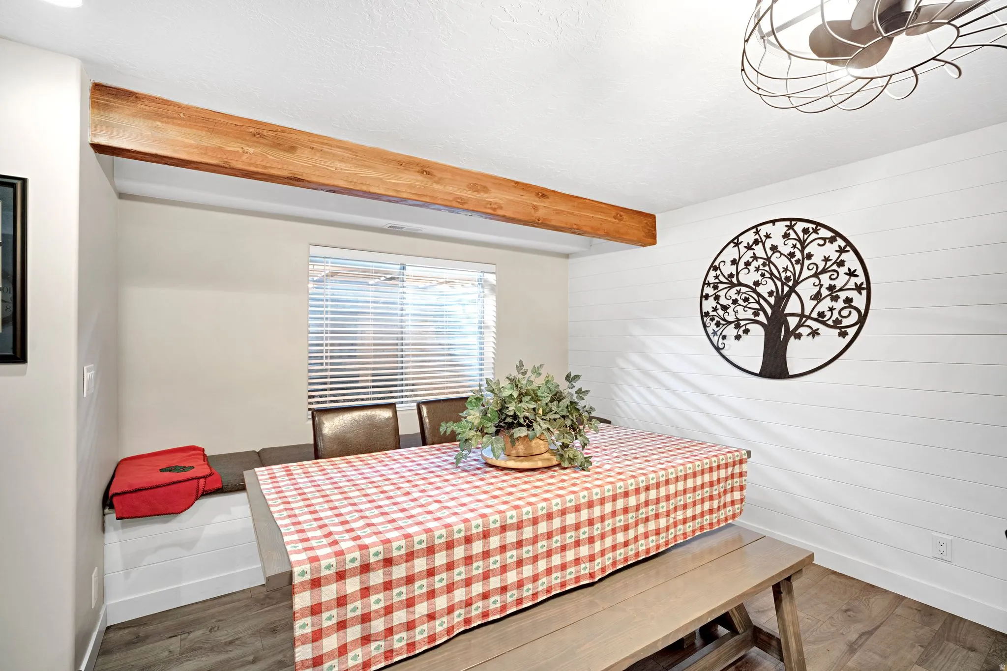Dining area featuring a prominent wood-finish beam, shiplap accent wall, built-in bench seating with storage underneath,  wood-finish flooring.